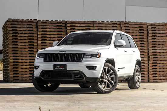 A white jeep grand cherokee is parked in front of a pile of wooden pallets.