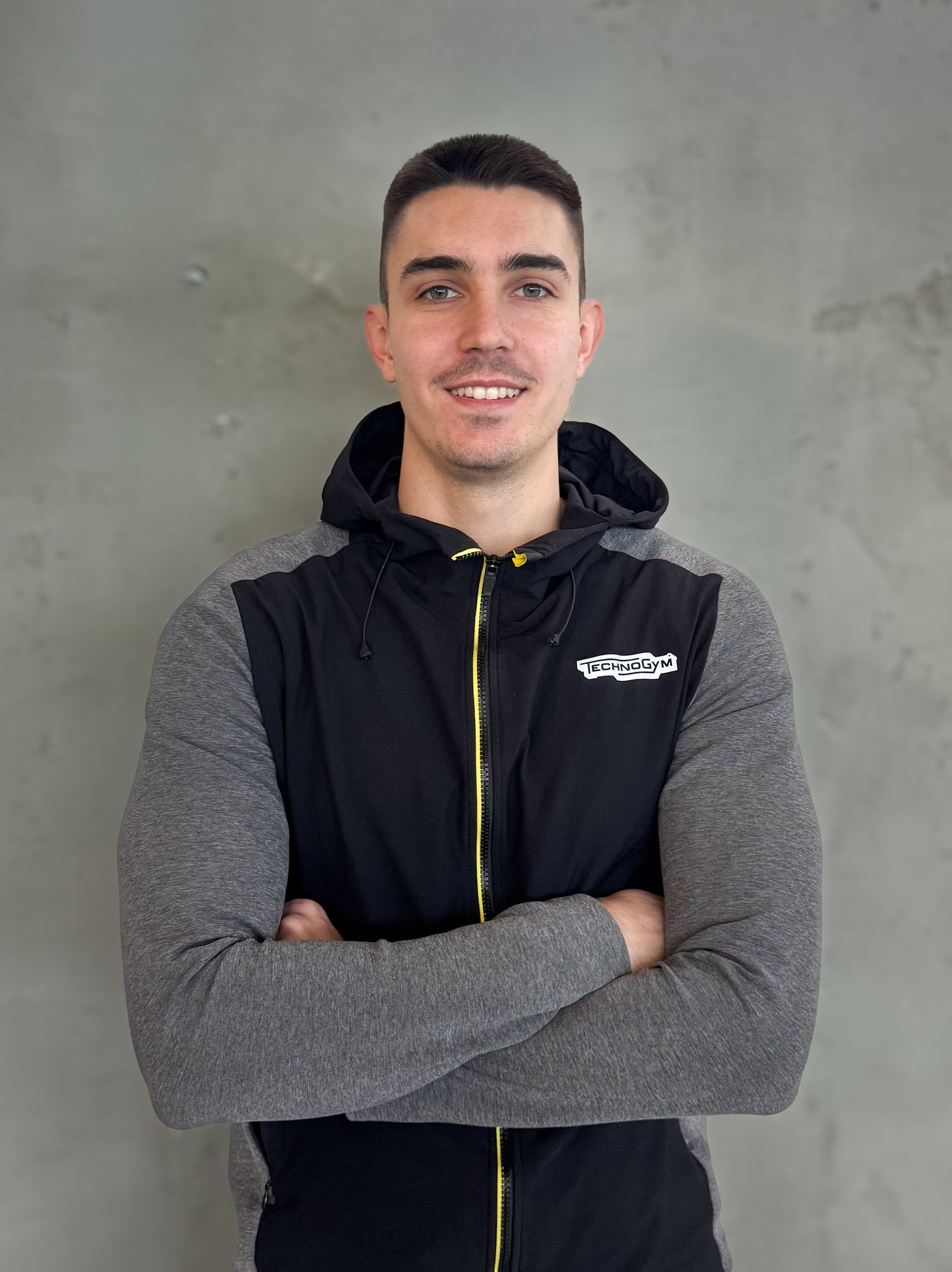 a man with his arms crossed is wearing a grey jacket with a yellow zipper