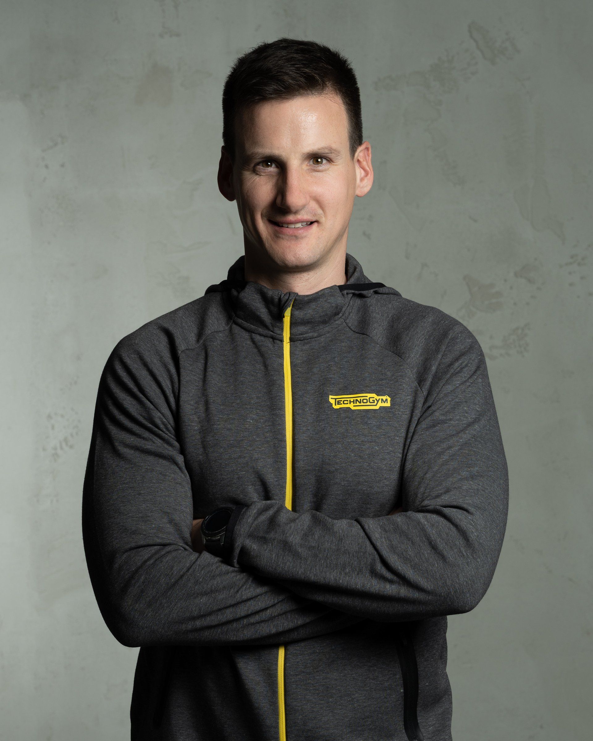 a man with his arms crossed is wearing a grey jacket with the word technogym on it