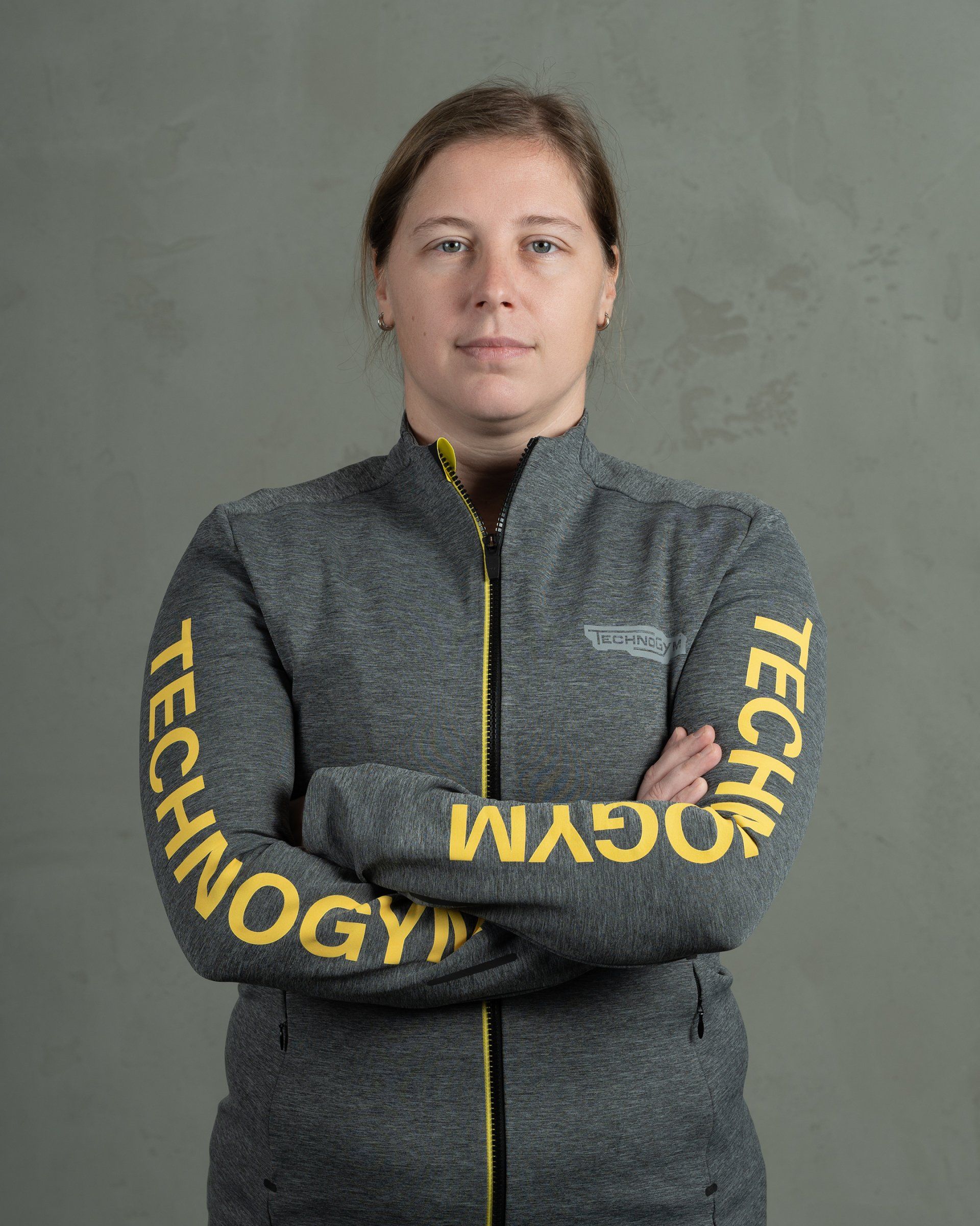 a woman with her arms crossed wearing a jacket that says technogym on the sleeves