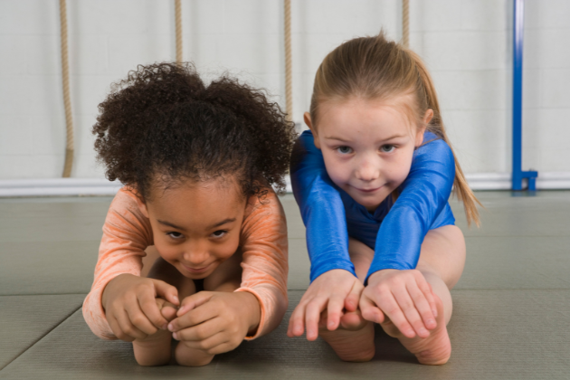 Two young girls are doing stretching exercises on the floor.