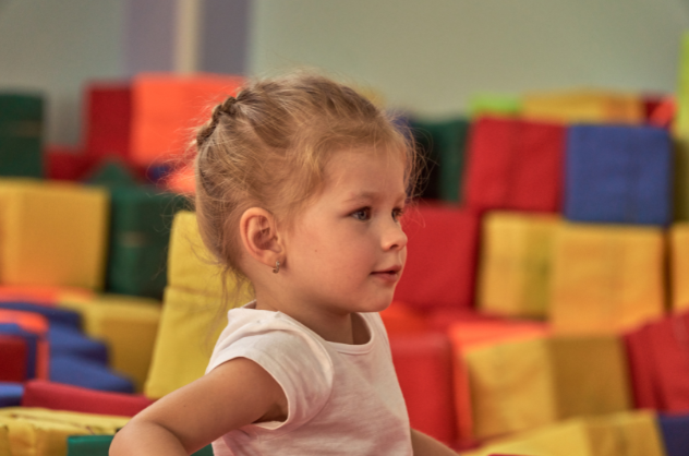 A little girl is standing in front of a pile of colorful blocks.