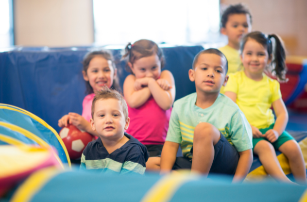 A group of children are sitting on a couch in a gym.