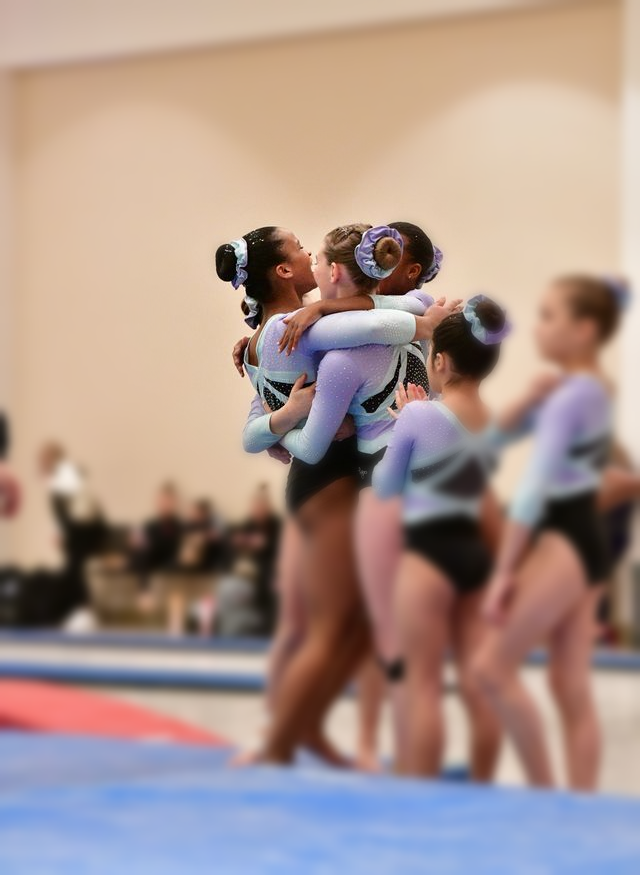 Cheer team in matching blue and black uniforms celebrating in an indoor gymnasium.