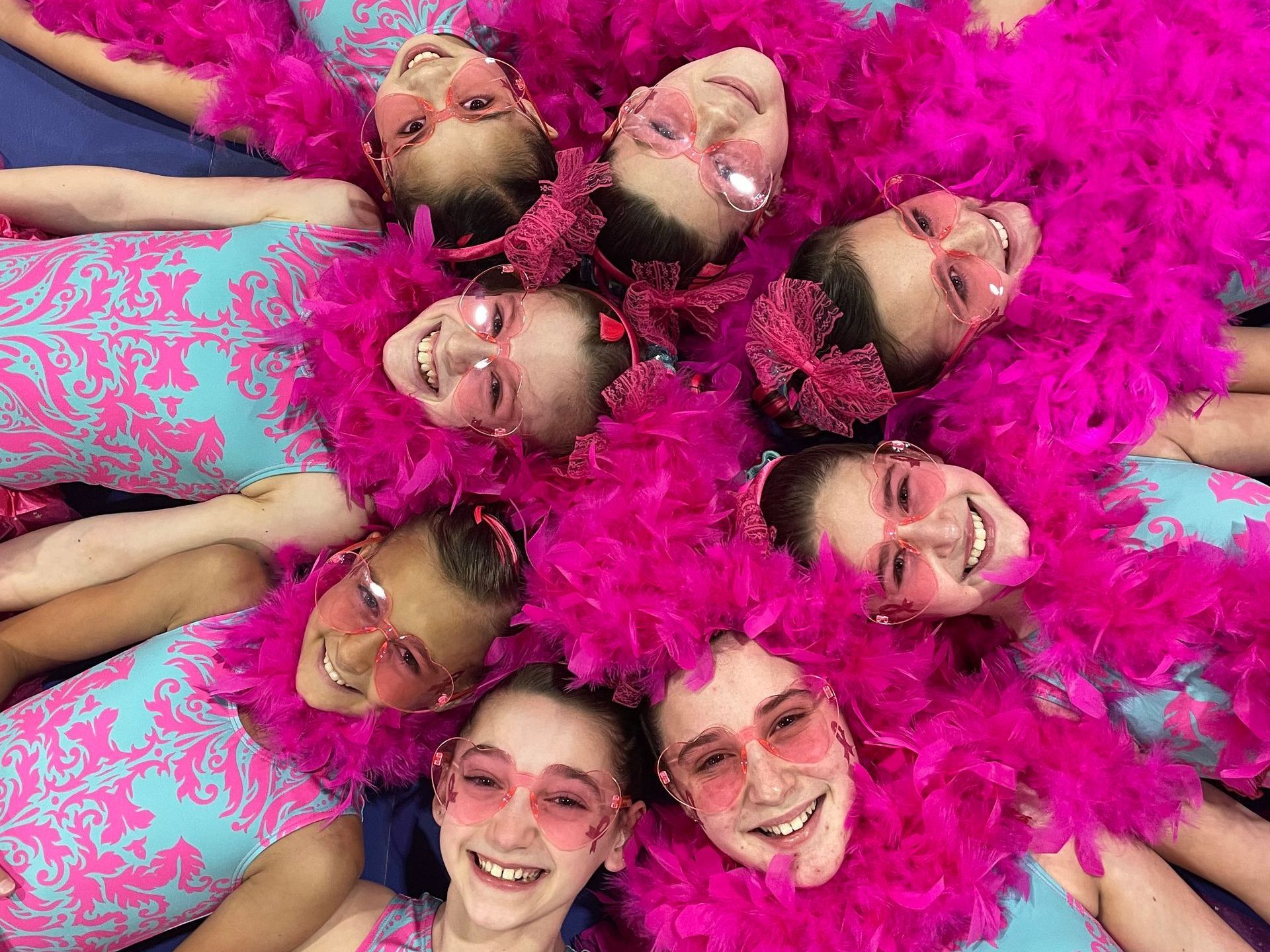 A group of young girls wearing pink feather boa and sunglasses are laying in a circle.
