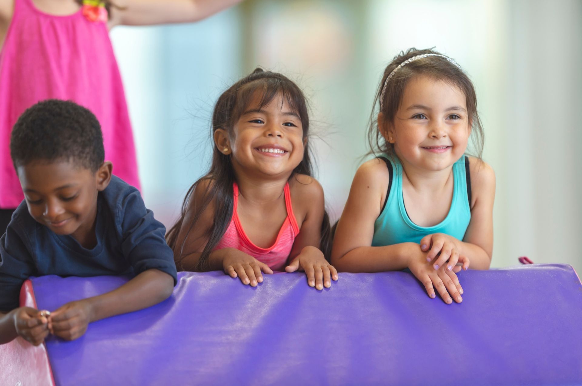 Three children are laying on a purple mat and smiling.