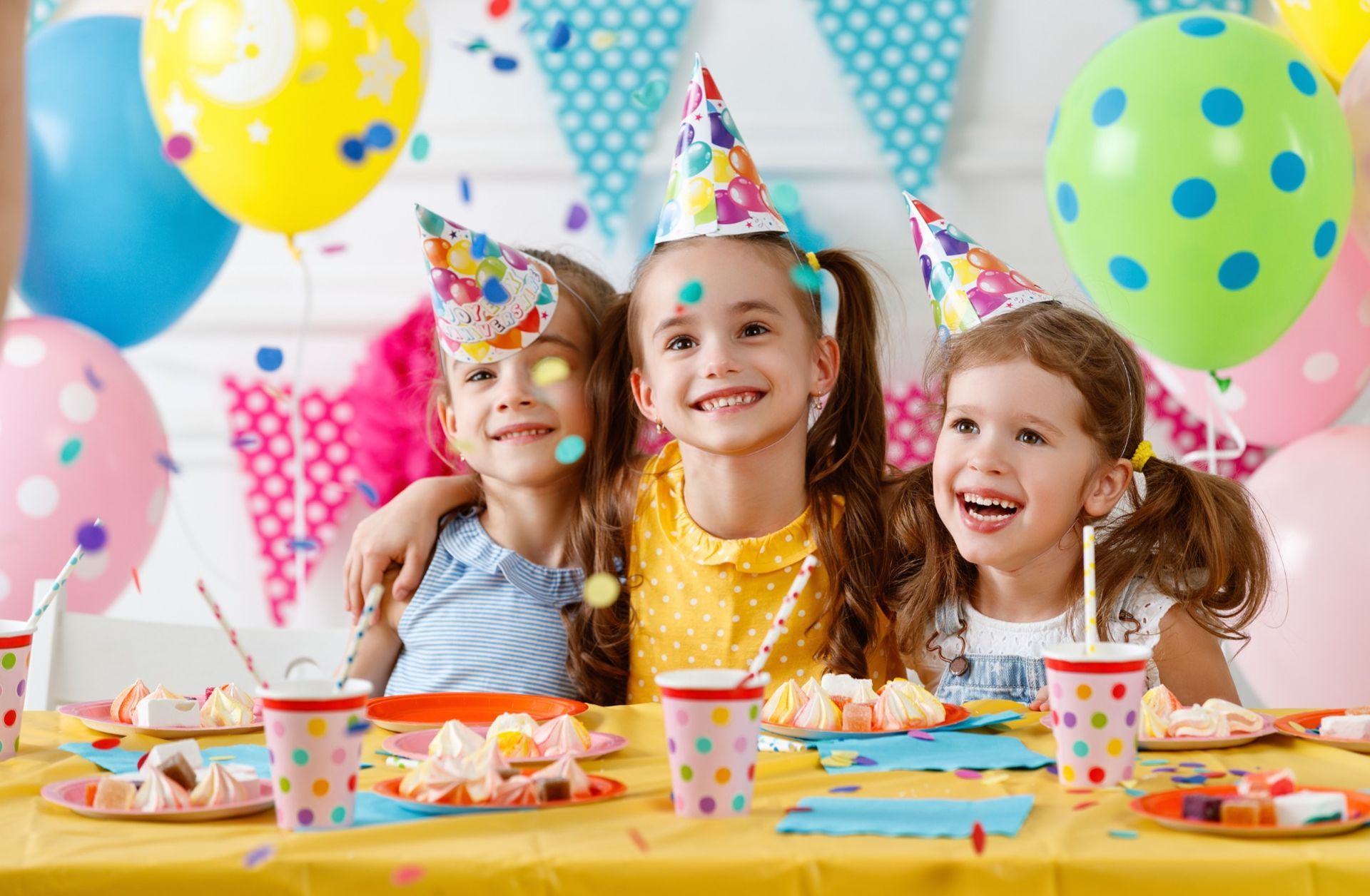 Three little girls are sitting at a table at a birthday party.