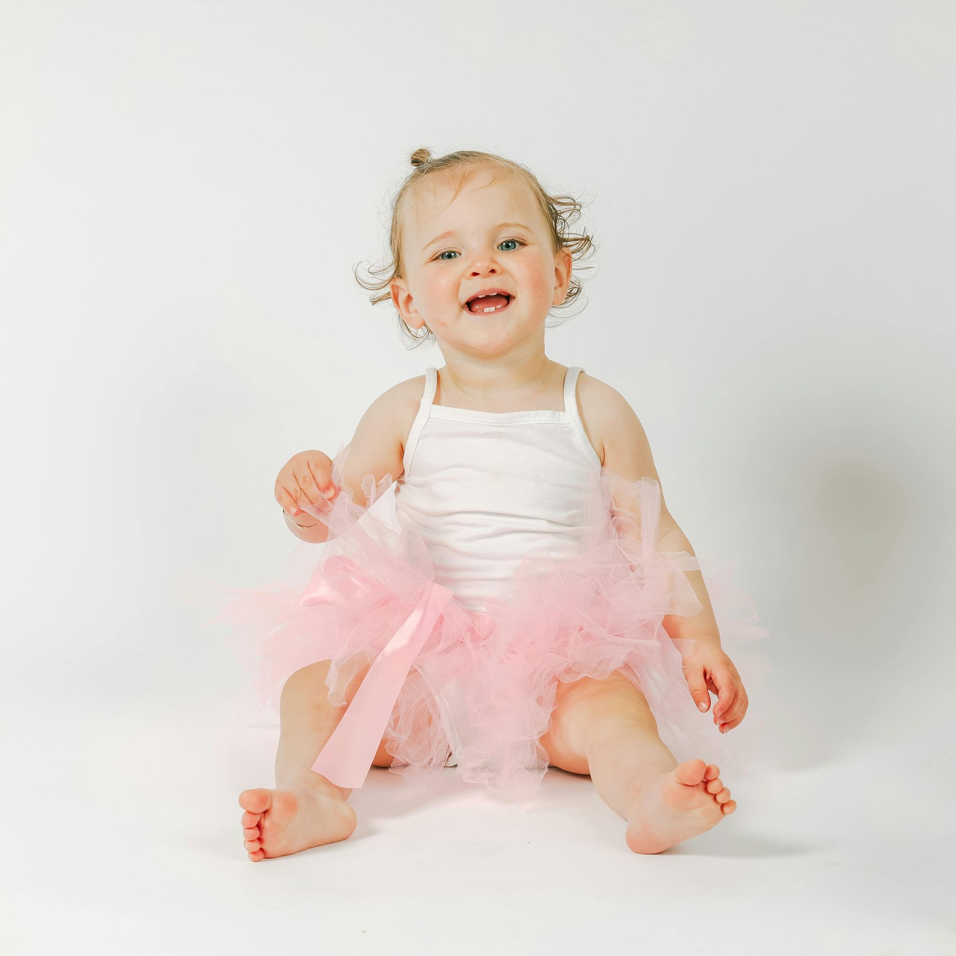 A baby girl is sitting on the floor wearing a pink tutu.