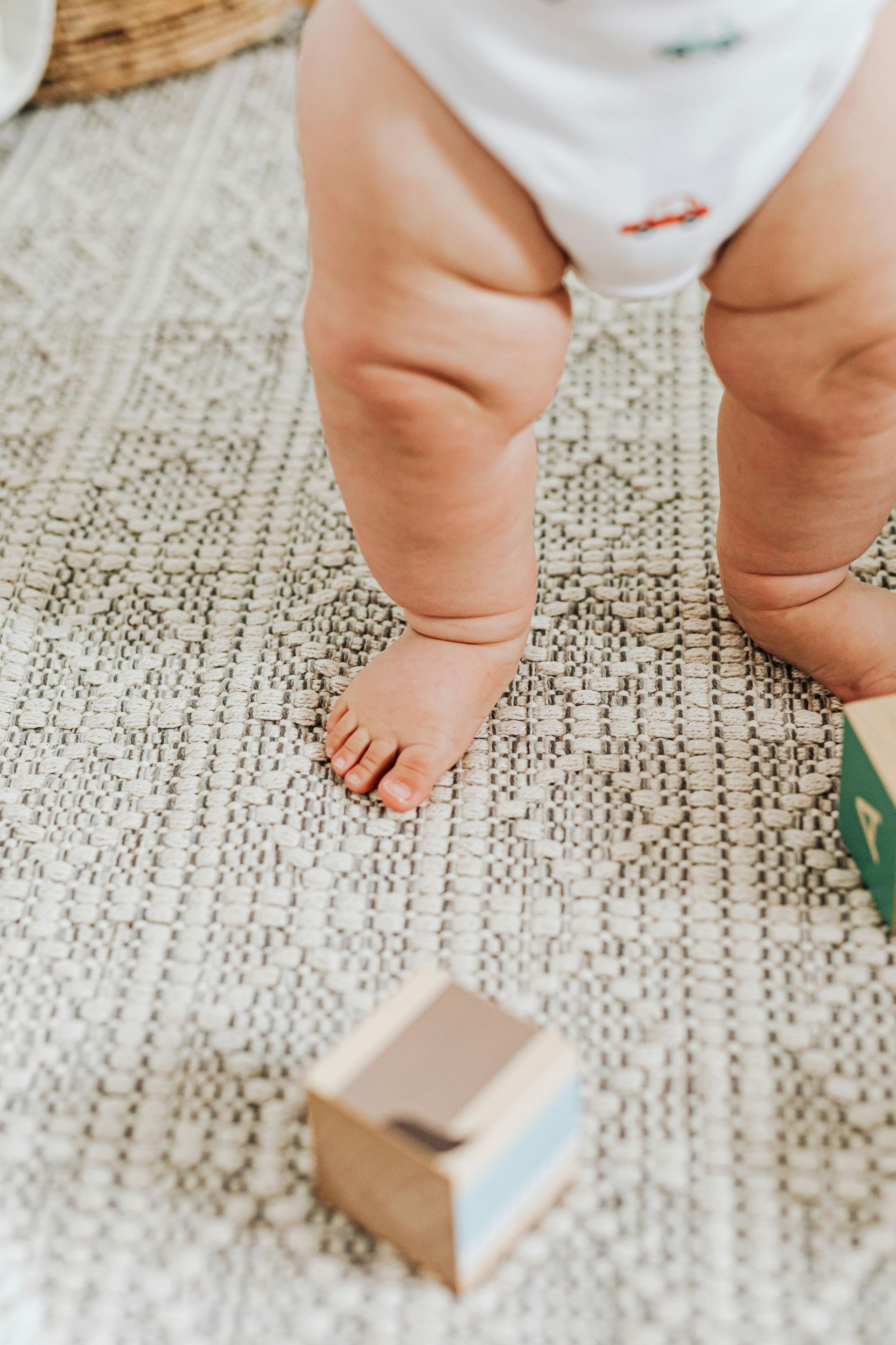 A baby is standing on a rug next to wooden blocks.