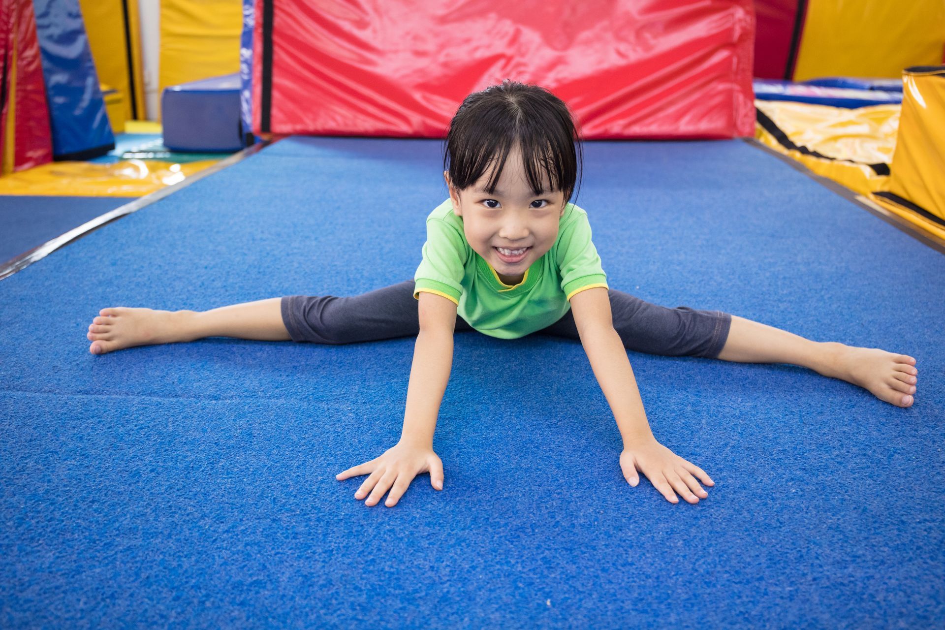 A little girl is doing a split on the floor in a gym.