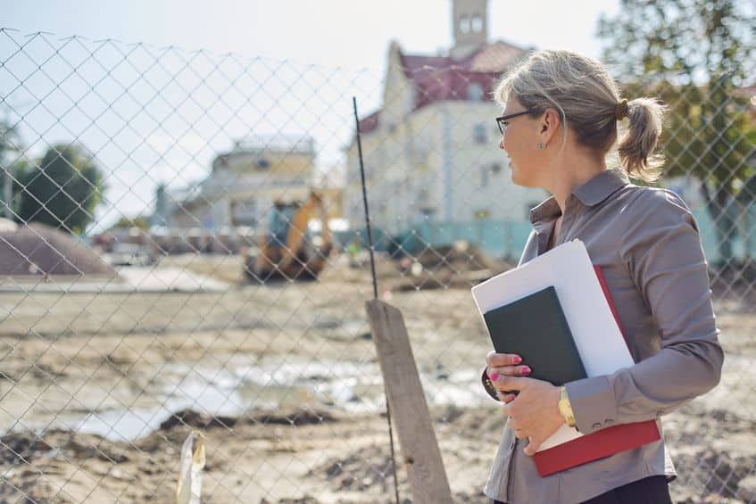 Woman wearing glasses at construction site, holding files, looking at the building.