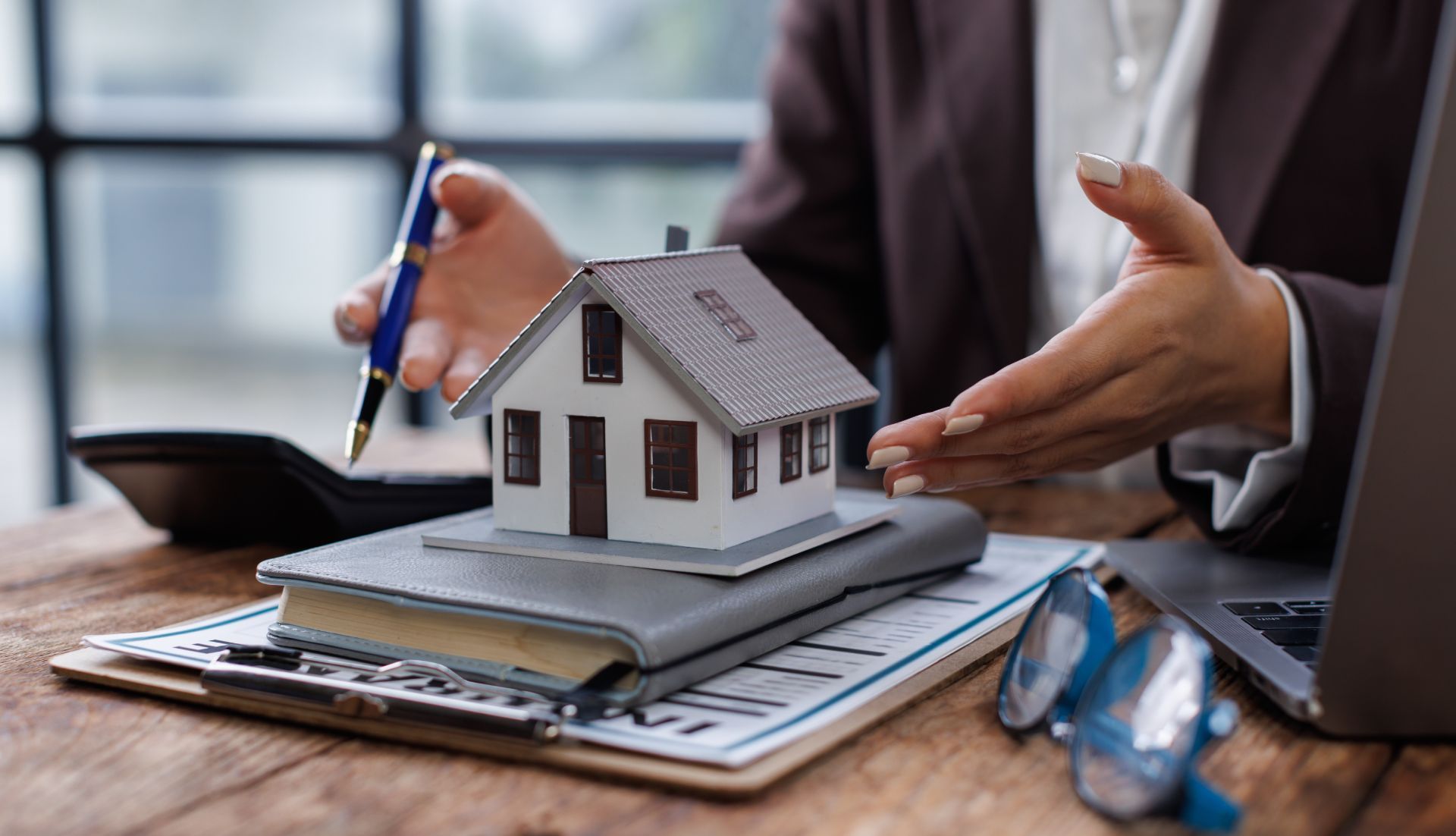 Person explaining a real estate deal, using a model house, documents, and laptop.