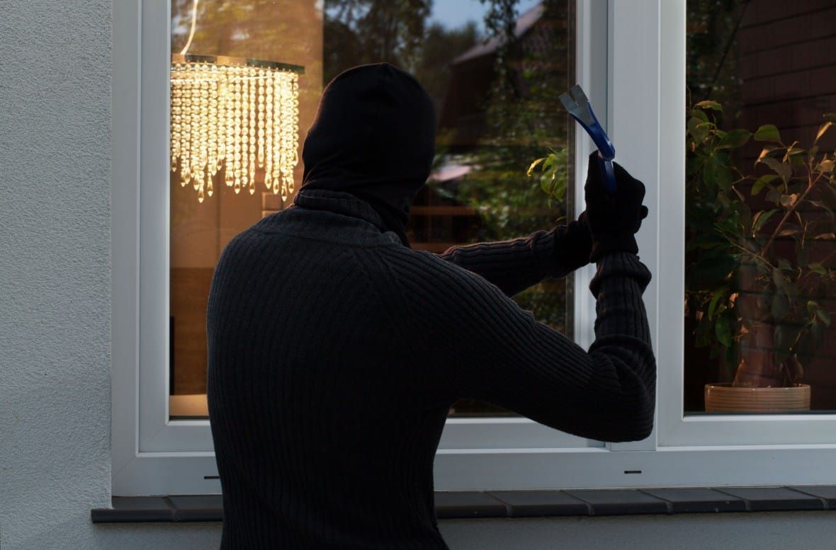 Person in dark clothing breaking window with a tool.