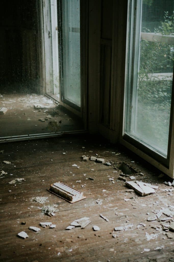 Interior corner of an abandoned room with broken debris on the floor and windows.