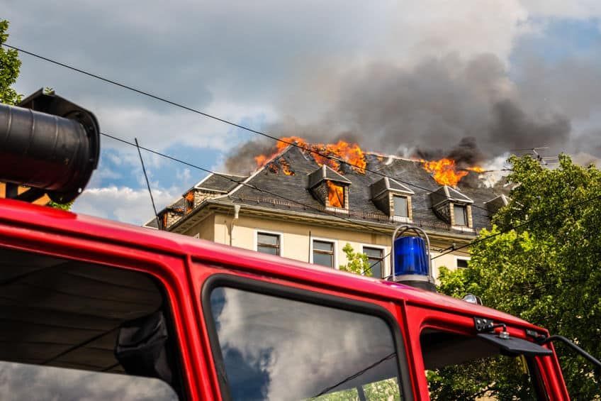 Fire truck in foreground, building on fire in background with flames and smoke.