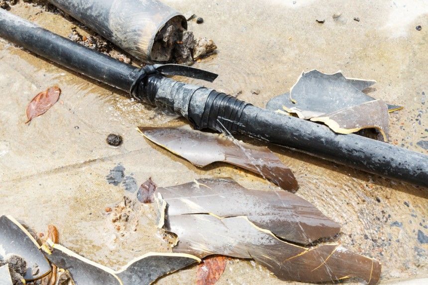 Broken black irrigation pipe and connector on concrete with debris.