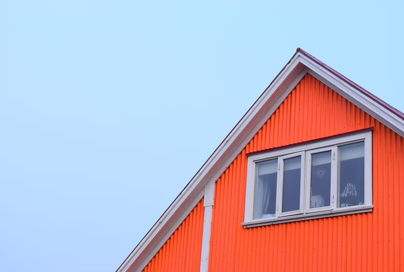 Orange house gable with white-framed window against a pale blue sky.