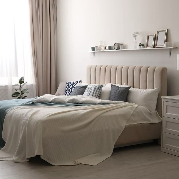 Beige-toned bedroom with a bed, plush headboard, bedside table, and window with curtains.