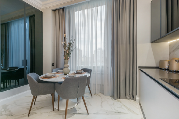 A dining area with a round white table, four gray chairs, marble floor, and long curtains in front of a window.
