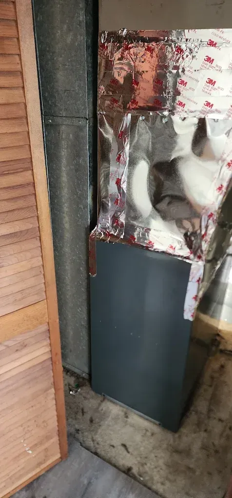 A dark gray HVAC unit wrapped with insulation in a room, next to a wooden door.
