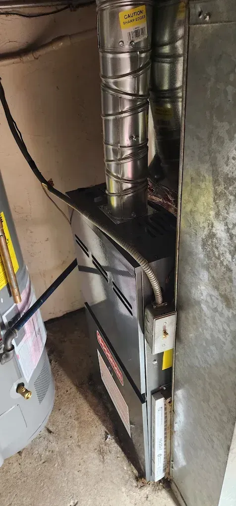 Furnace in a basement; silver metal with vents, ductwork, and water heater.