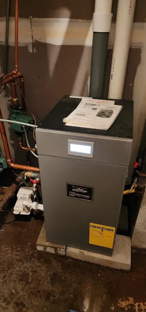 A gray heating system in a basement with pipes and a yellow energy-efficient sticker.
