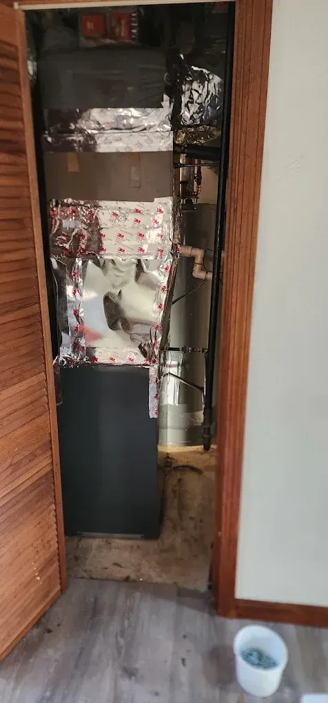 Open closet with HVAC unit, ductwork, and insulation visible. Brown door and trim, light-colored walls, and gray floor.