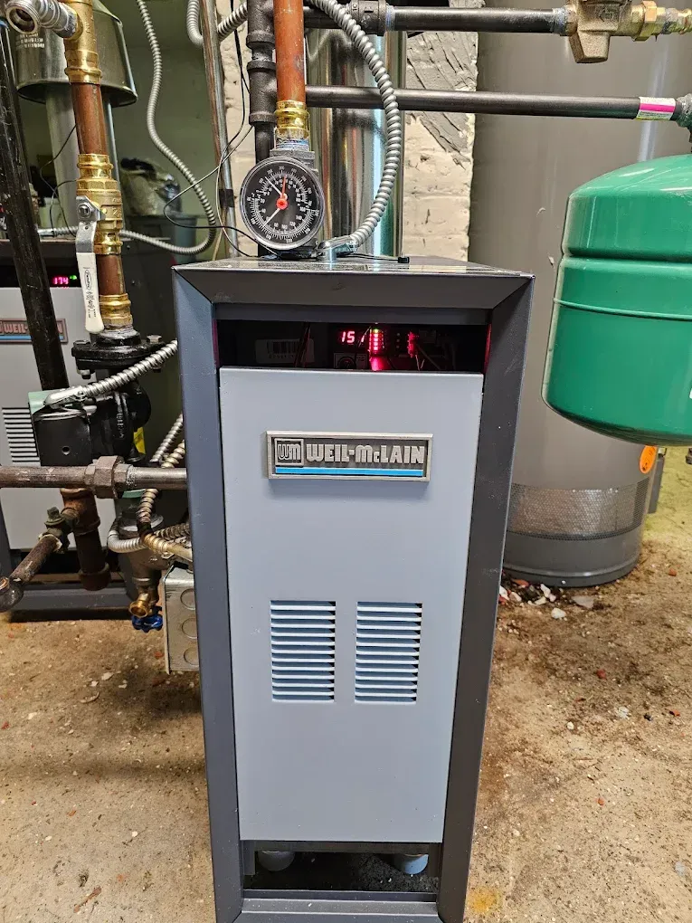 A gray and black boiler with a pressure gauge and other connected plumbing.