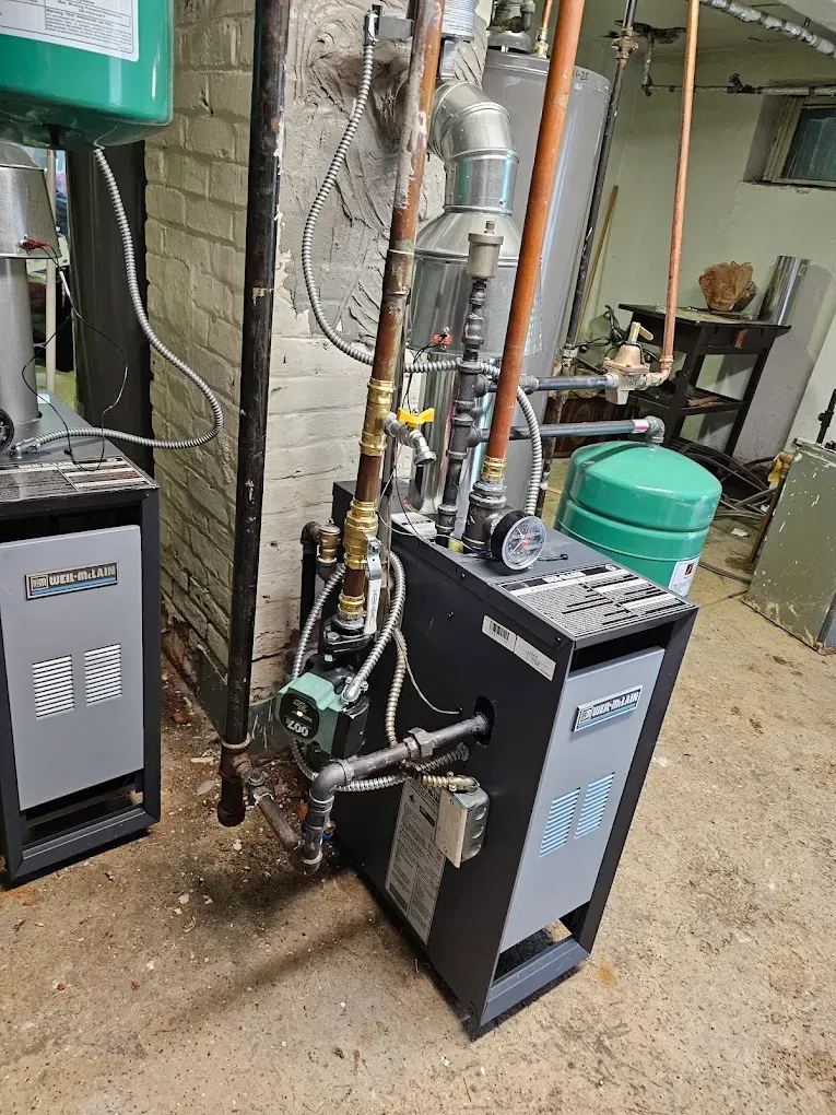 Two heating boilers in a basement. Copper pipes and a green expansion tank are also visible.