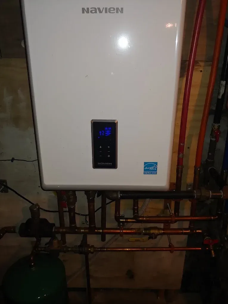 Navien tankless water heater, white, mounted on a wall with copper pipes.