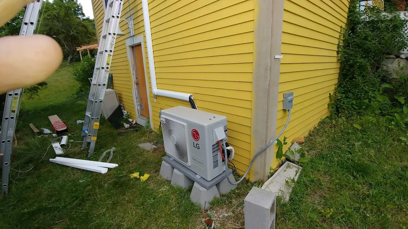 Yellow house with AC unit on concrete blocks, ladder, and tools on grass.