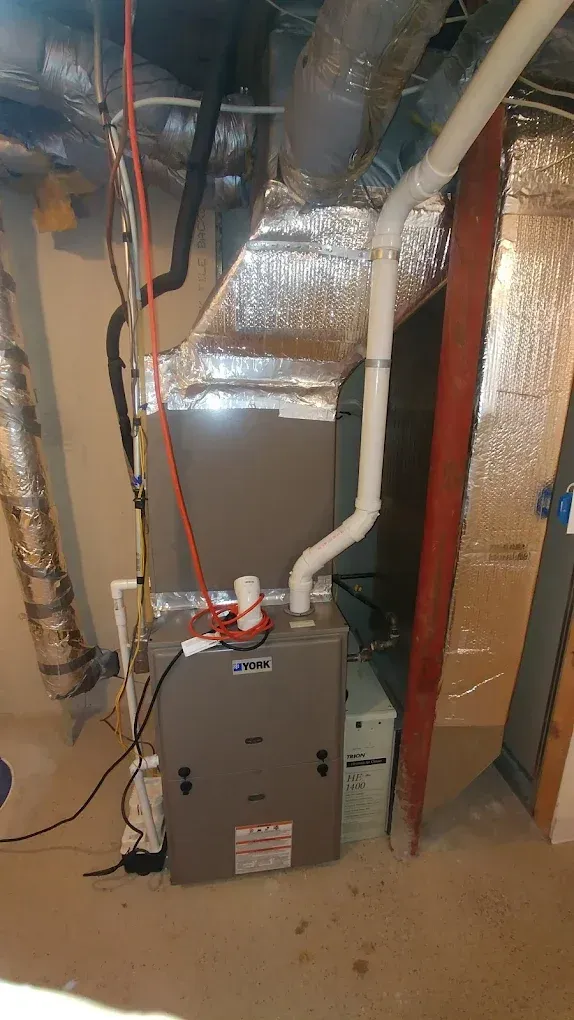 Furnace and HVAC system in a basement. Metal and white components with ductwork.