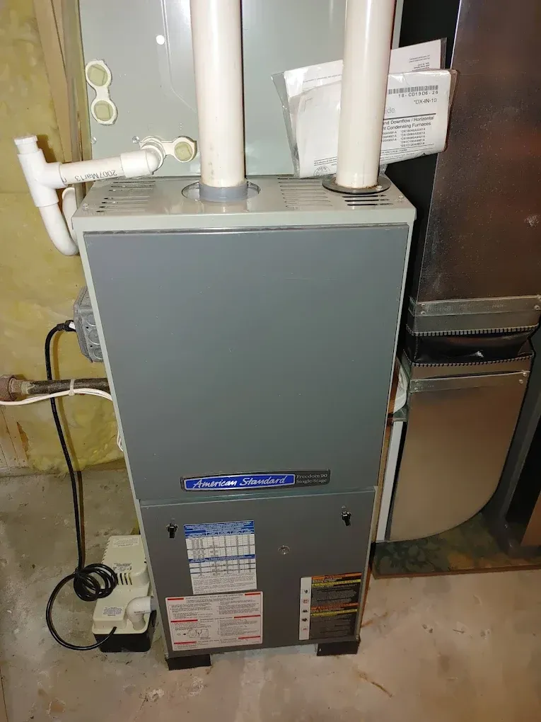 Gray furnace with white PVC pipes in a basement setting.