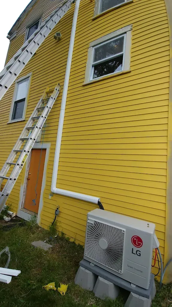 Yellow house with ladders, orange door, and LG air conditioning unit on gray blocks.