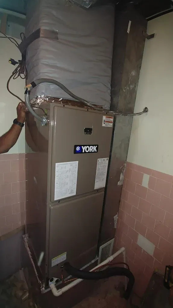 York HVAC system in a room with pink tiled wall, a person's arm on the side.