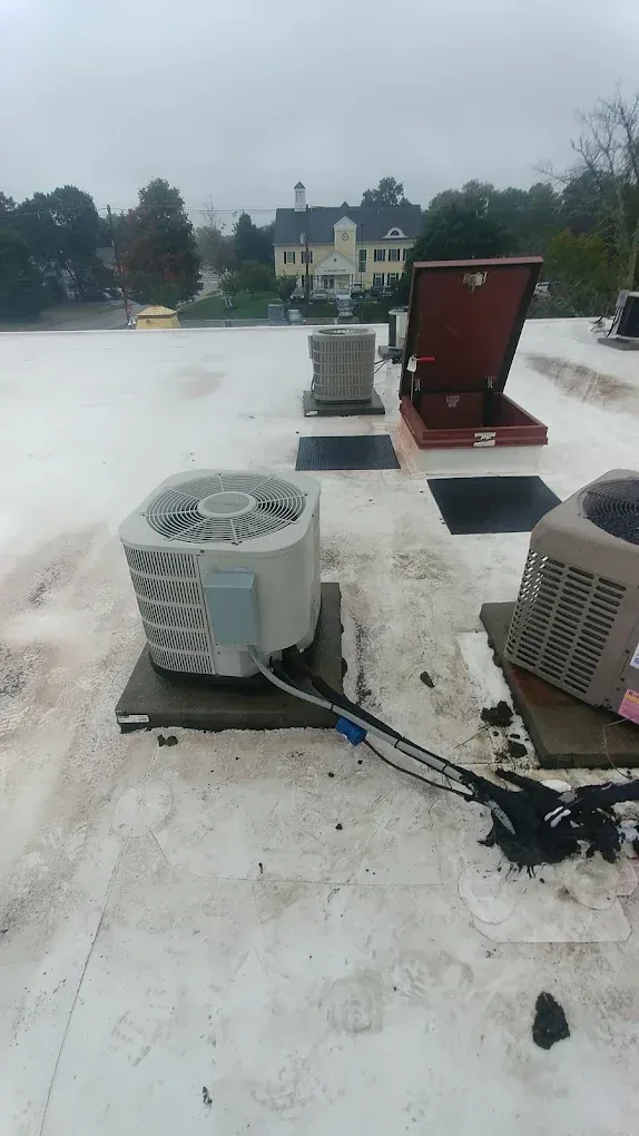 AC units on a flat white roof with a red open hatch, and a cloudy sky.