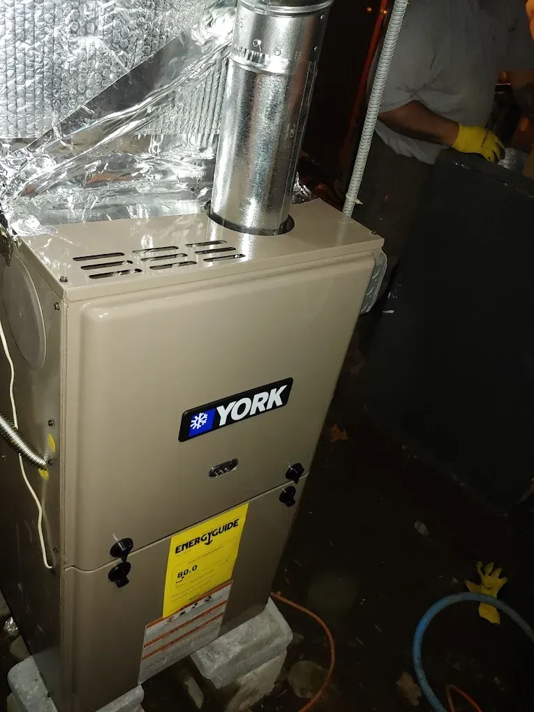 Tan York furnace with silver vent pipe, installed in a utility room. Yellow energy sticker on front.