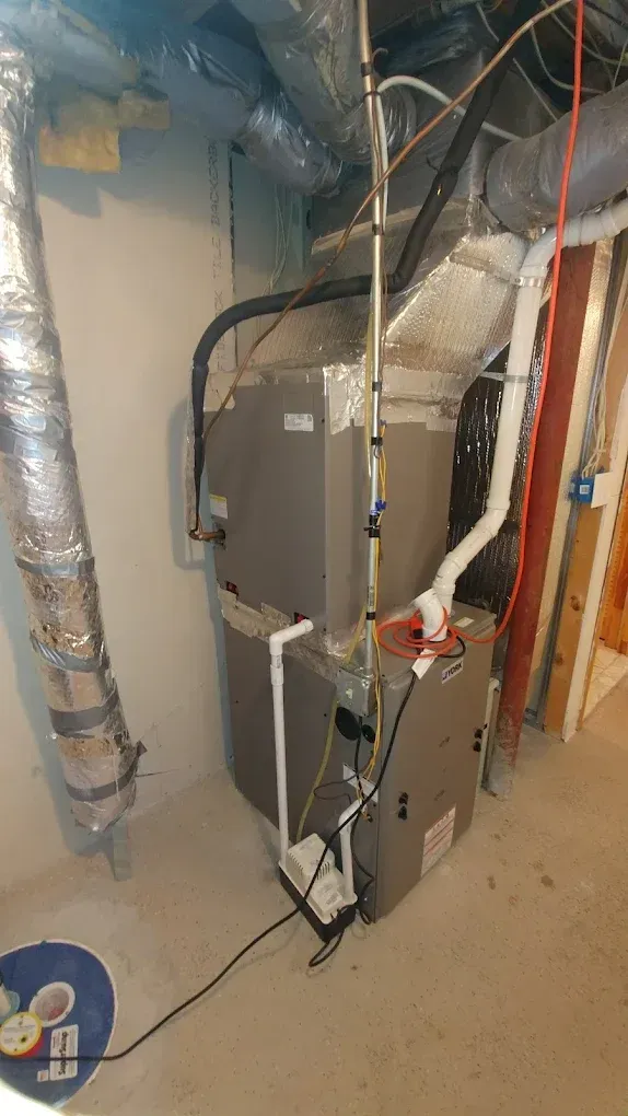 HVAC unit in a basement. Metal and silver ductwork, pipes, and electrical components. Grey and silver.
