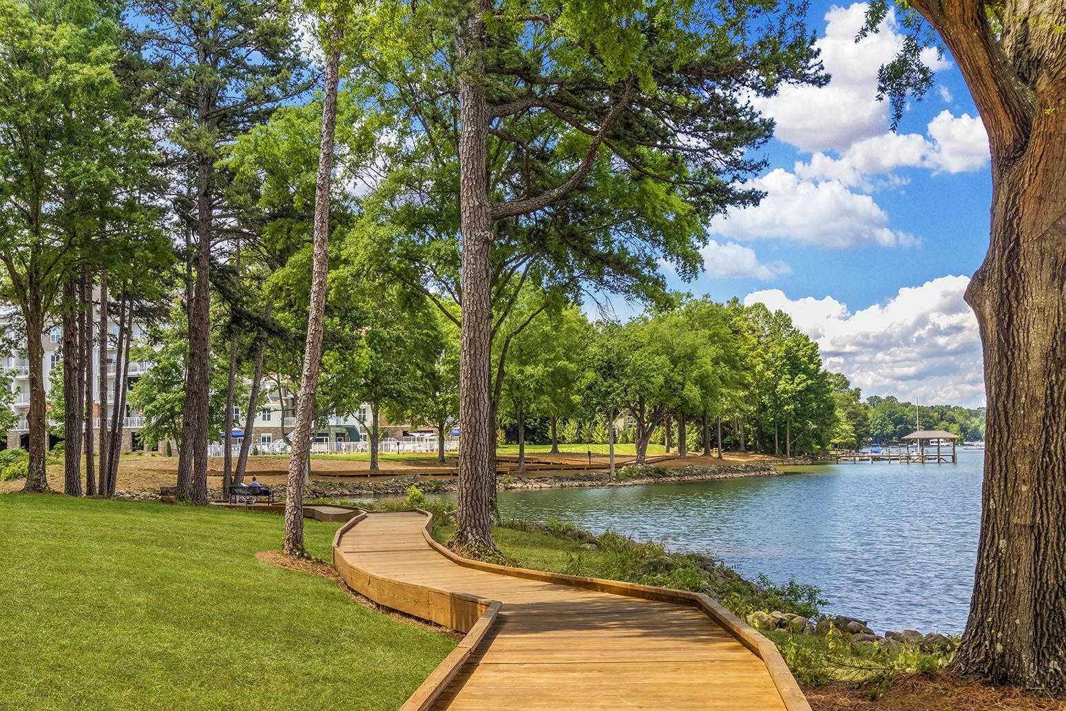 A wooden walkway leading to a lake surrounded by trees at The Osprey in Mooresville, NC.