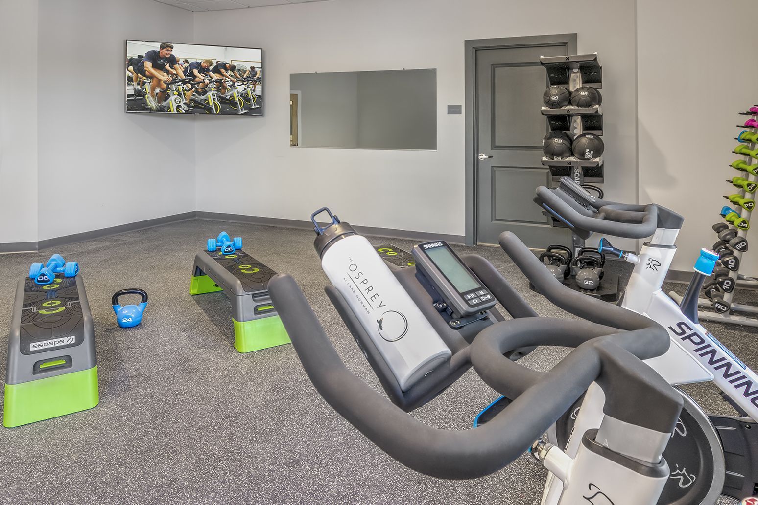 A gym with exercise bikes , dumbbells , and a television at The Osprey in Mooresville, NC.