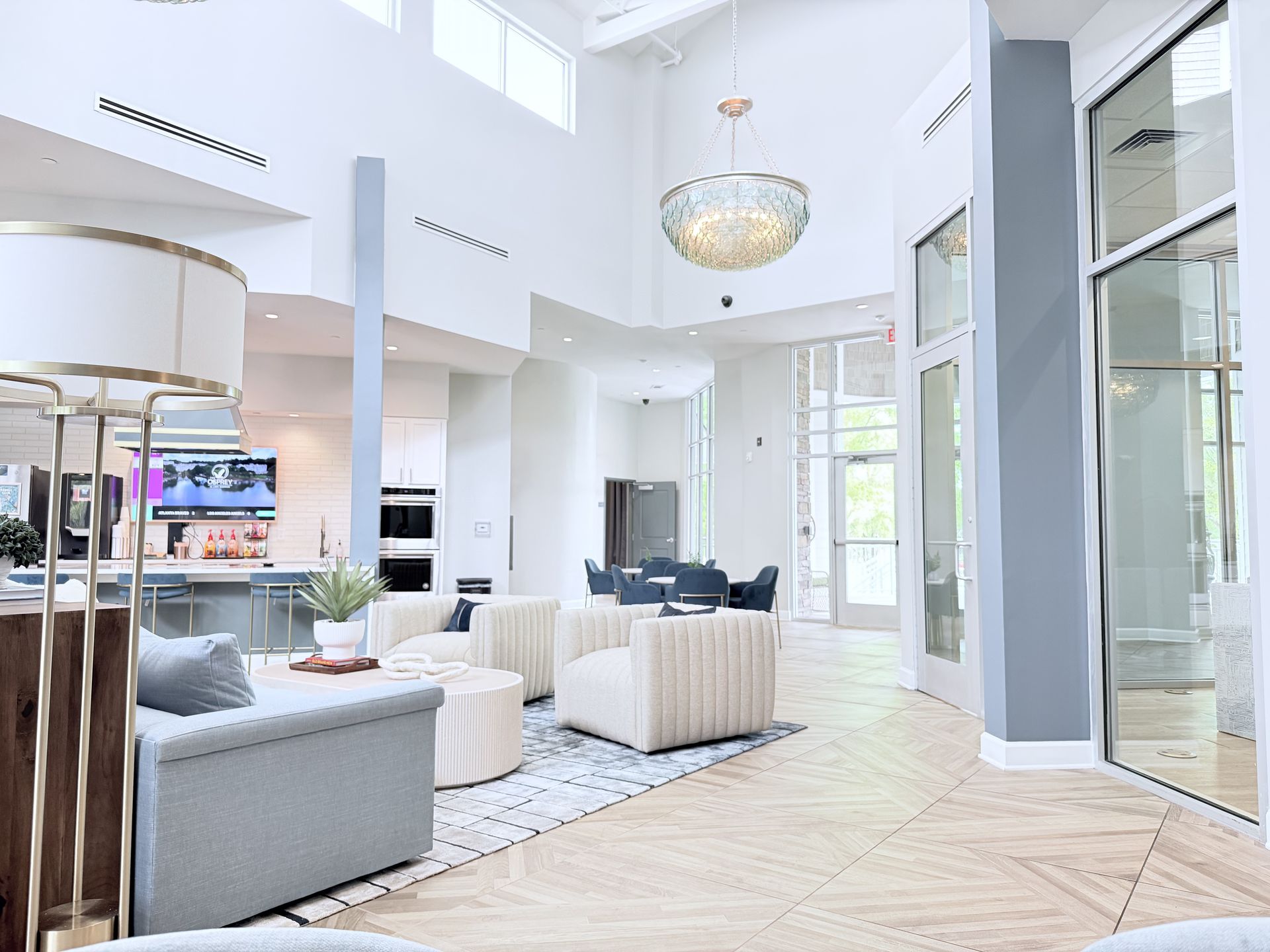 Bright modern living room with high ceilings, white walls, gray and beige seating, and a crystal chandelier