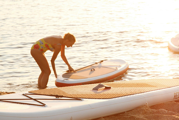 A woman in a bikini is putting a paddle board into the water.