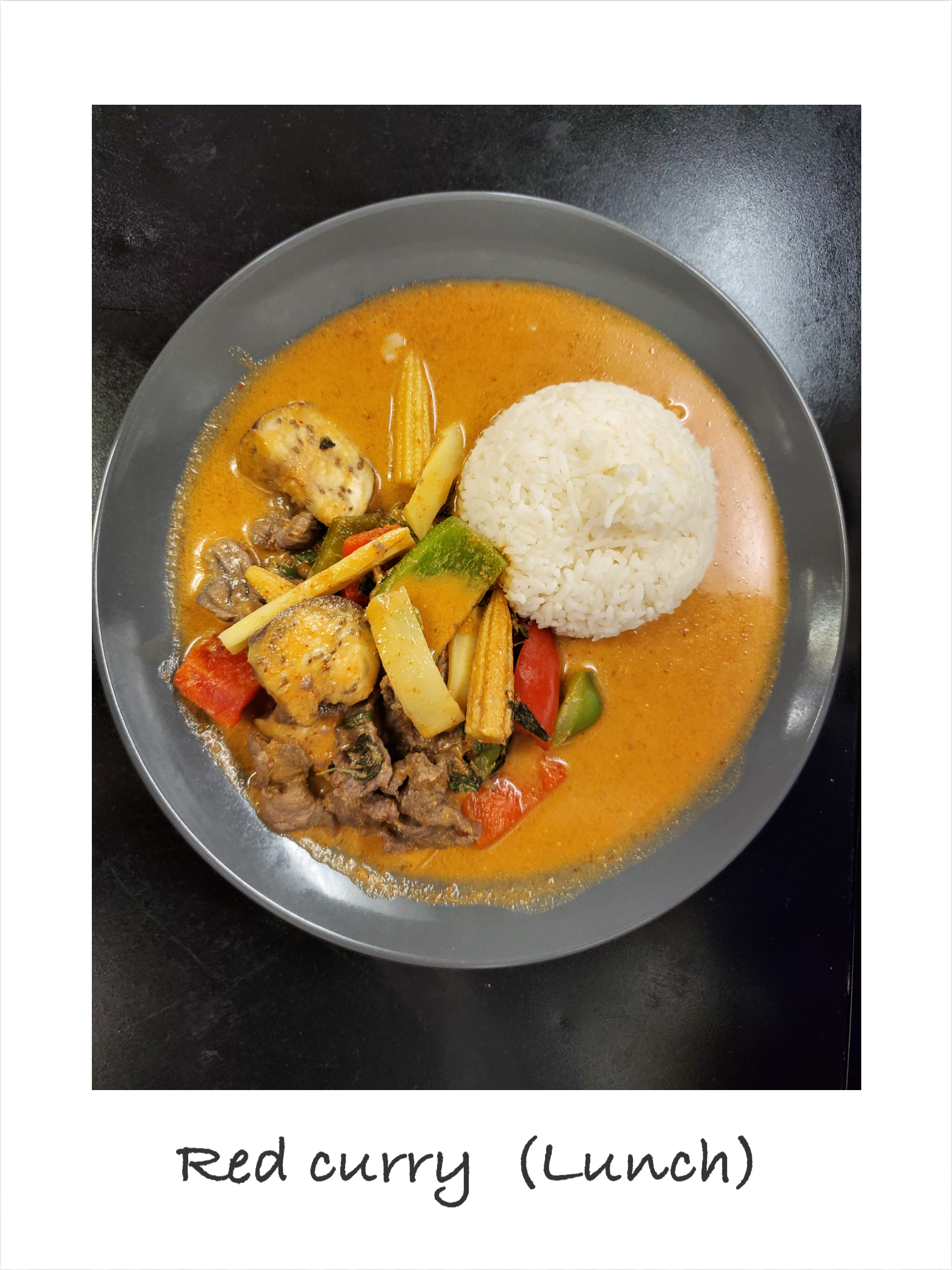 A bowl of red curry with rice and vegetables on a table.