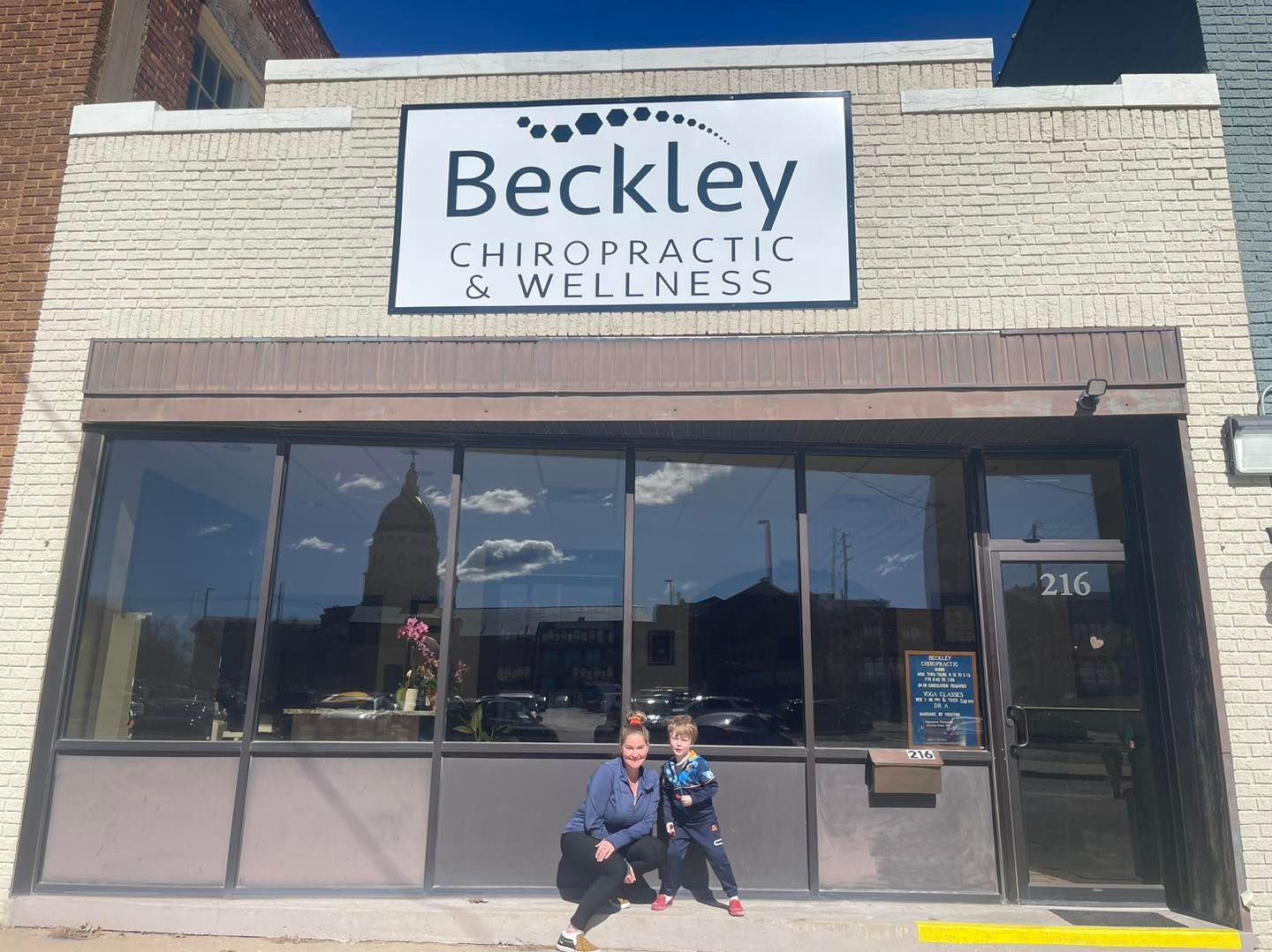 Two children are sitting in front of a building that says beckley chiropractic and wellness.
