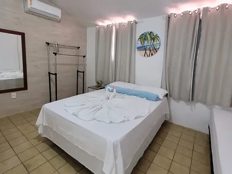 Quarto com cama de casal, espelho, cabideiro, ar-condicionado e decoração de parede com tema de praia.