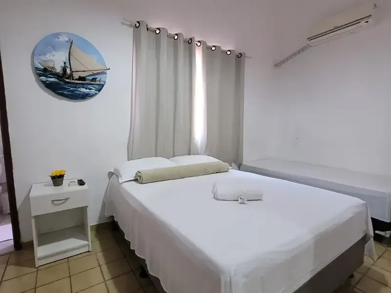 Quarto com cama branca, mesa de cabeceira, decoração com tema de veleiro e um pequeno berço.