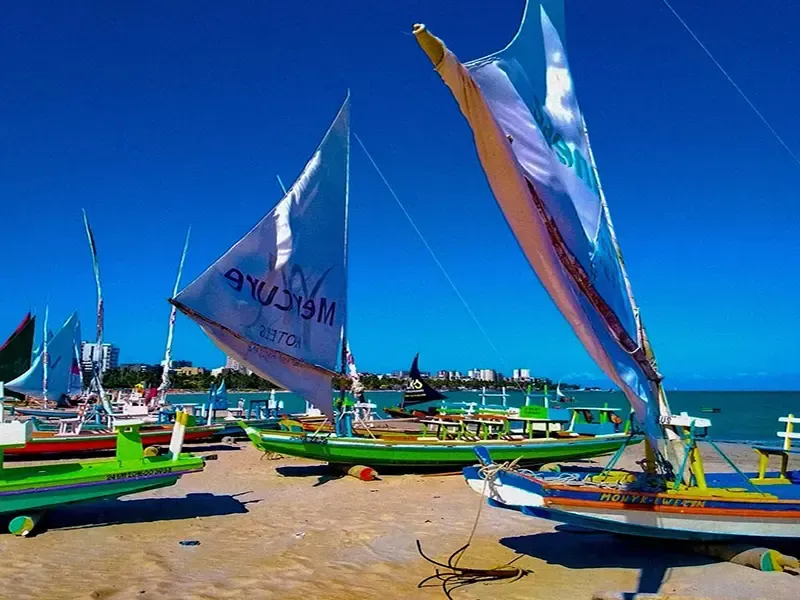 Barcos de pesca coloridos com velas em uma praia ensolarada, céu azul claro acima.