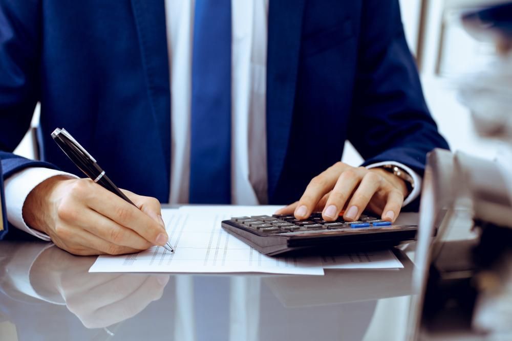 A Man in a Suit is Writing on a Piece of Paper While Using a Calculator — SouthMac Finance In Townsville, QLD