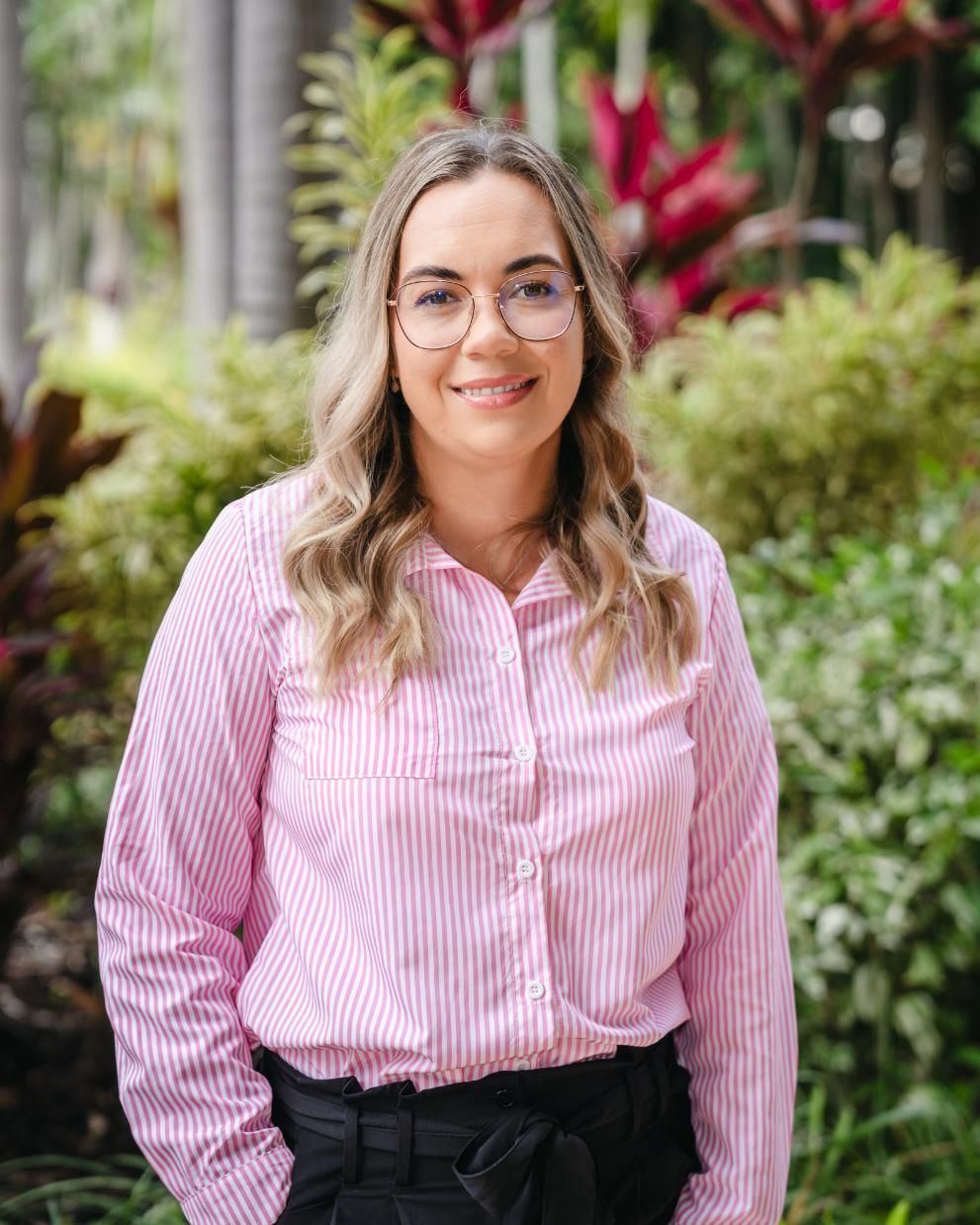 A Woman Wearing Glasses and a Pink Striped Shirt is Standing in Front of a Garden — SouthMac Finance In Townsville, QLD