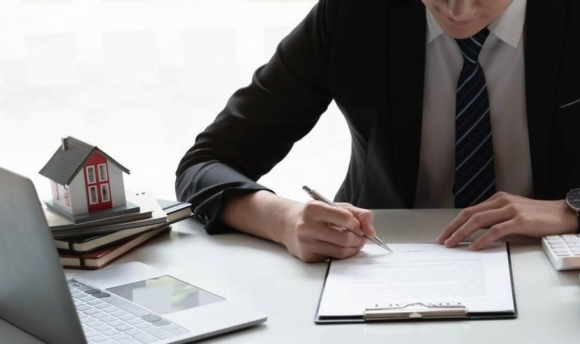 A Man in a Suit and Tie is Sitting at a Desk Signing a Document — SouthMac Finance In Townsville, QLD